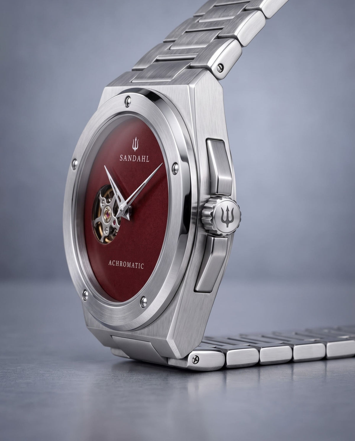 Angled view of the SANDAHL ACHROMATIC Crimson, showing its red dial, steel case, crown and steel bracelet.