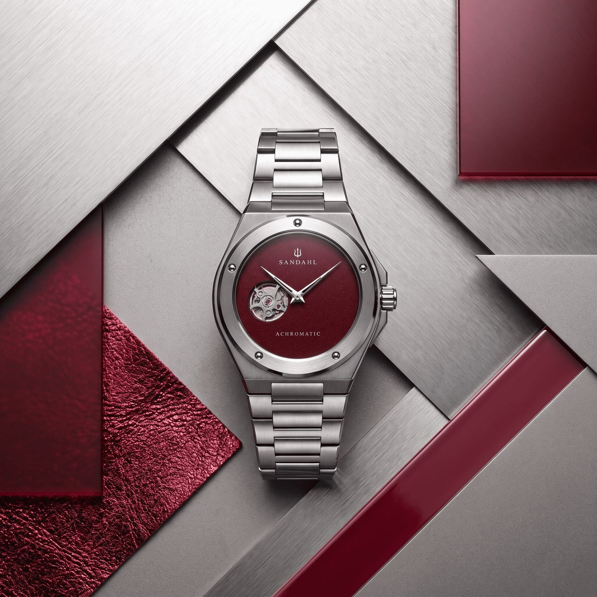 SANDAHL ACHROMATIC Crimson with a steel bracelet, arranged among red, silver and white material.