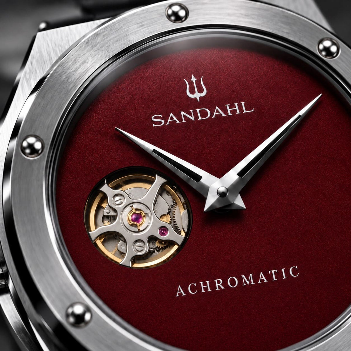 Close-up of the red SANDAHL ACHROMATIC Crimson dial, open-heart aperture, polished hands and trident.