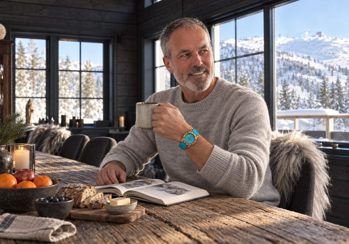 Man wearing a glacial aqua SANDAHL AEREUS bronze watch while enjoying morning coffee at a wooden table overlooking snowy Åreskutan.