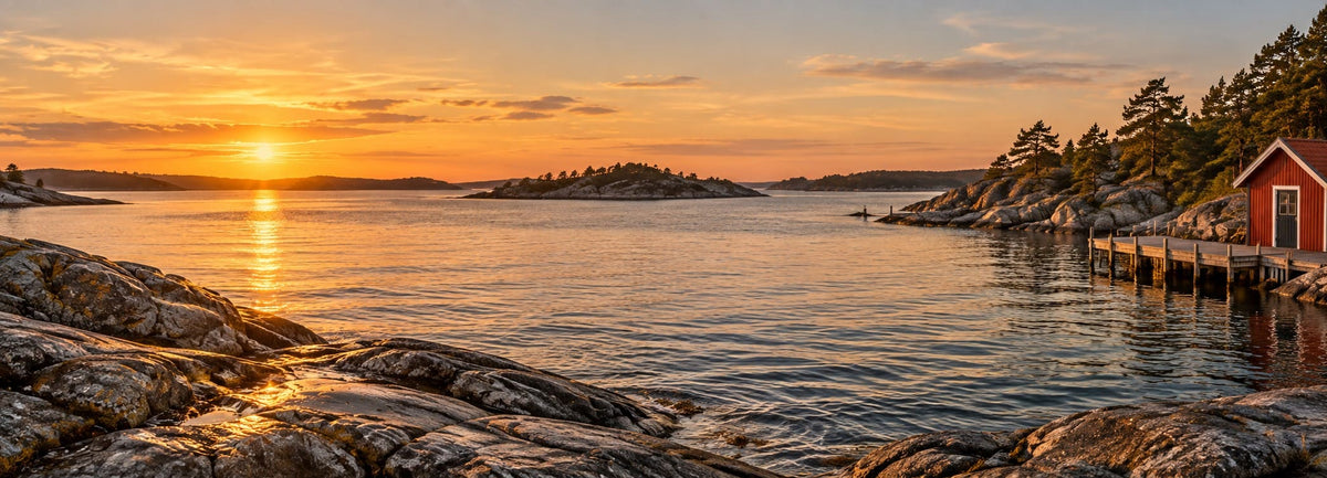 Golden sunset over the Swedish archipelago, with granite rocks, pine-covered islands and a red boathouse beside a wooden jetty.