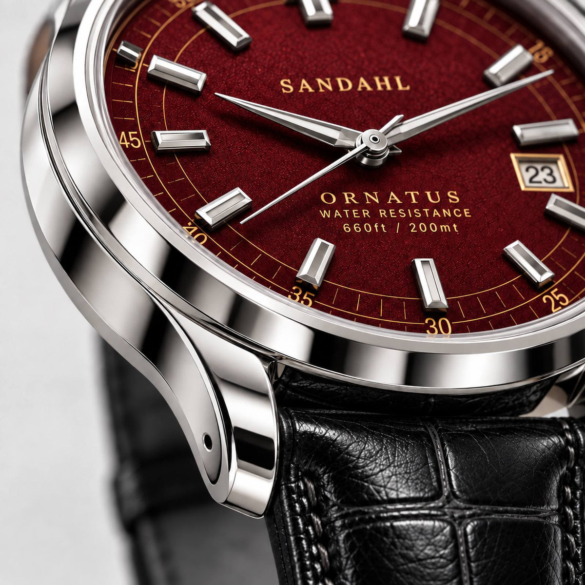 Close-up of the polished steel case and rounded lugs of SANDAHL ORNATUS Garnet, with a red textured dial and black leather strap.