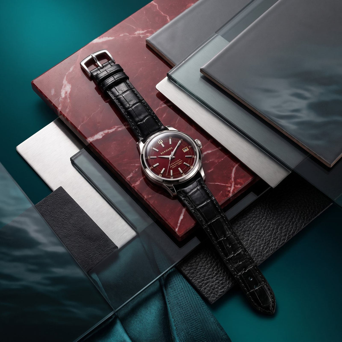 SANDAHL ORNATUS Garnet with a burgundy-red dial and black crocodile-pattern leather strap, arranged with red stone, glass and brushed metal material samples.