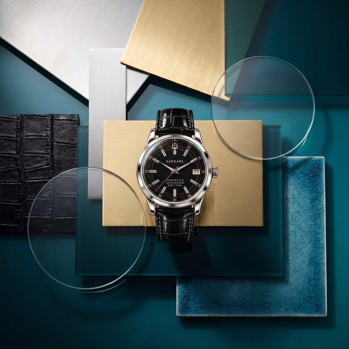 SANDAHL ORNATUS Onyx with a black dial and black crocodile-pattern leather strap, arranged with glass, leather and metal material samples on a teal background.