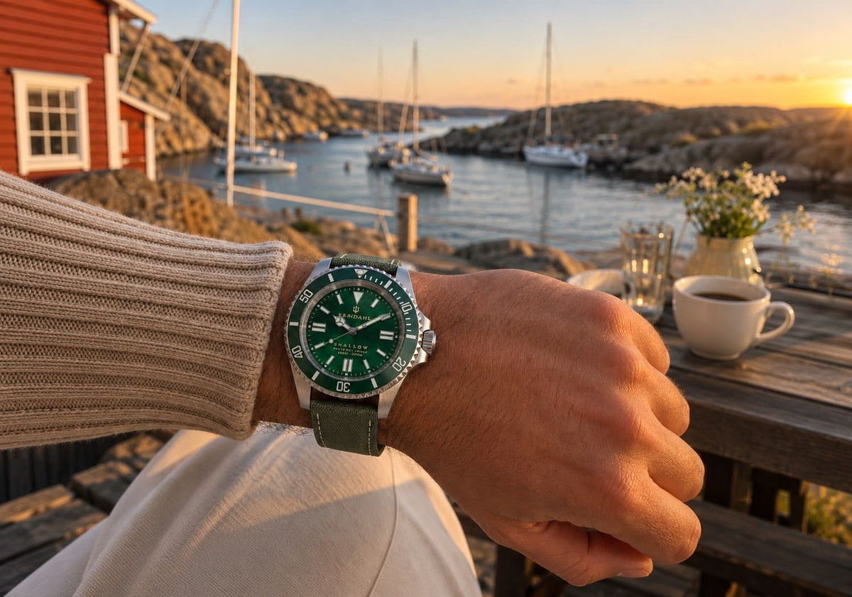 SANDAHL SHALLOW Archipelago Green worn beside a red coastal cottage overlooking a harbour at sunset.