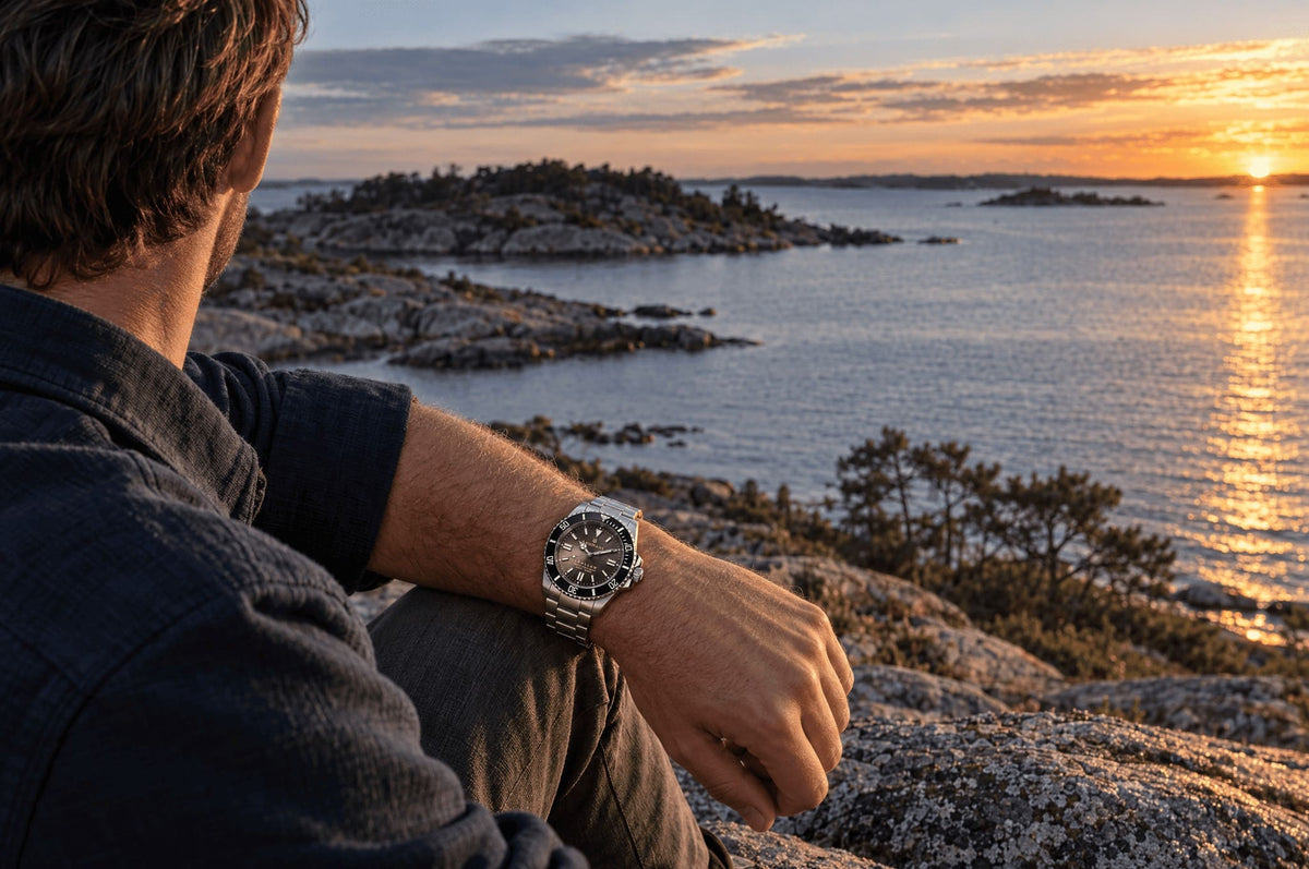 SANDAHL SHALLOW Granite Grey worn while seated on coastal rocks overlooking the Swedish archipelago at sunset.