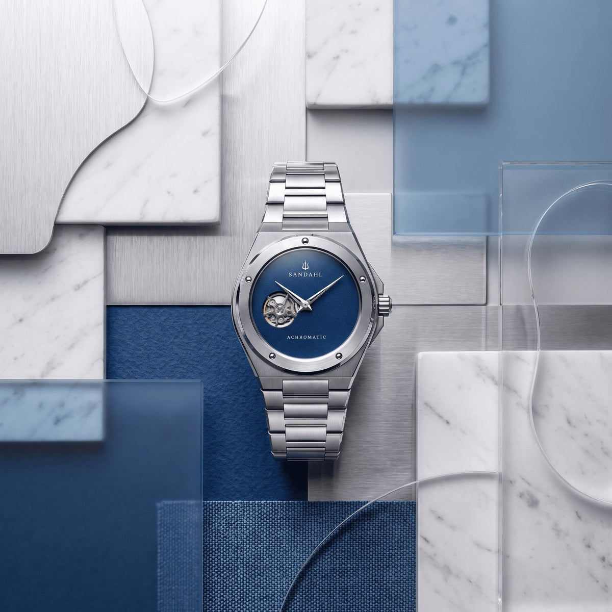 SANDAHL ACHROMATIC Cobalt with a steel bracelet, arranged among blue, silver and white material samples.