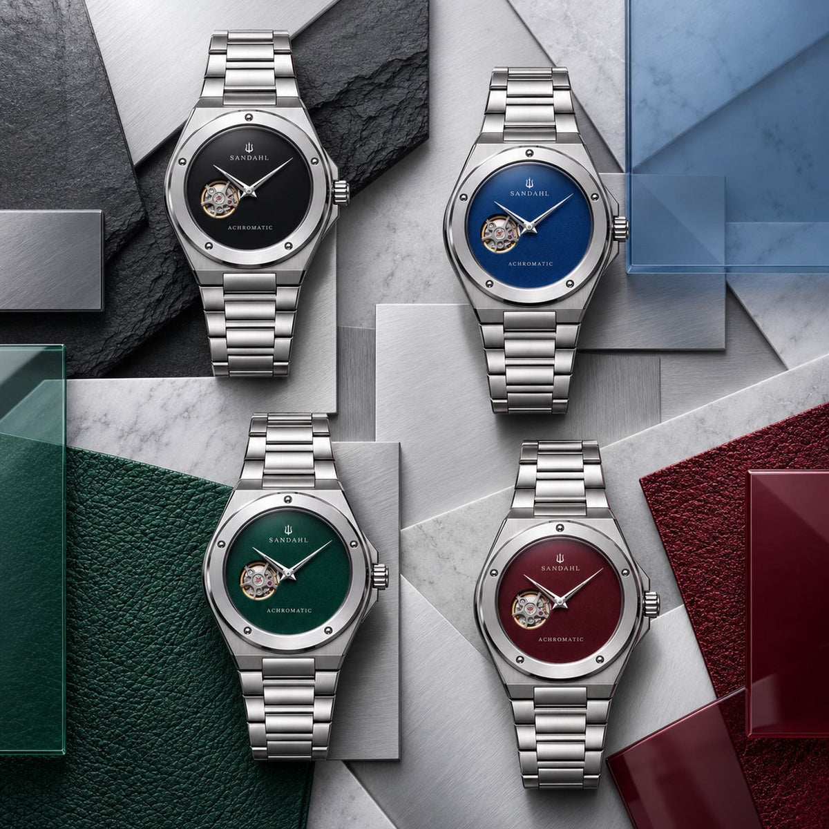 Four SANDAHL ACHROMATIC watches with black, blue, green and burgundy dials, arranged on brushed steel with matching glass, leather and slate accents.