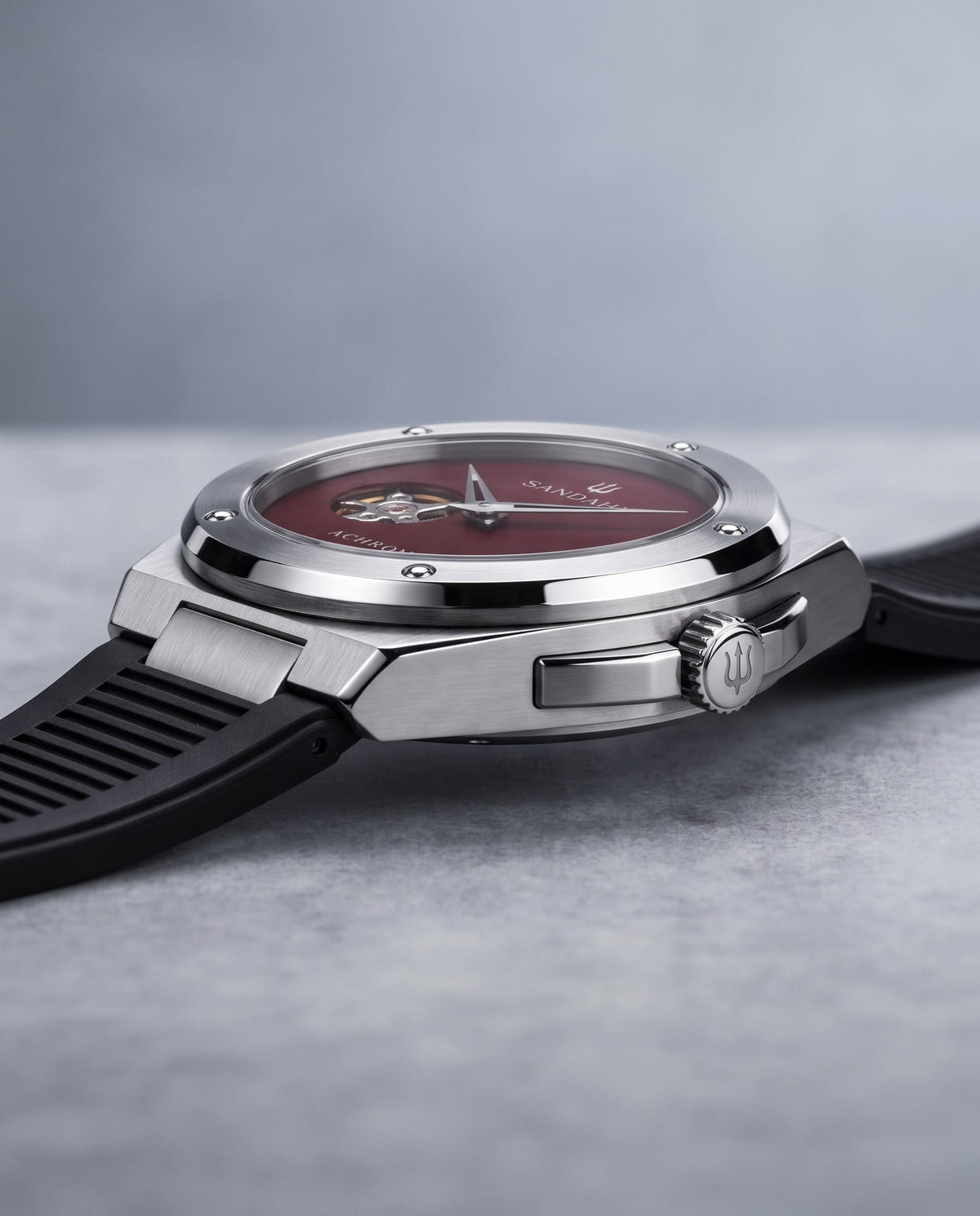 Angled view of the SANDAHL ACHROMATIC Crimson with a red dial, steel case and black rubber strap.