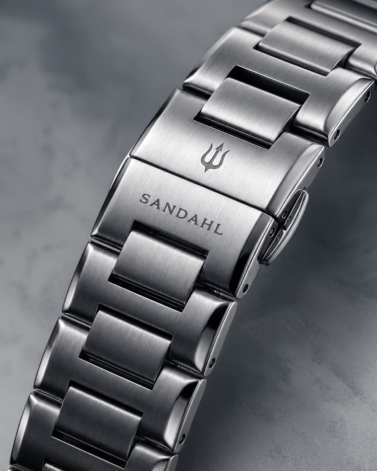 Close-up of the SANDAHL ACHROMATIC steel bracelet clasp, engraved with SANDAHL and the trident logo.