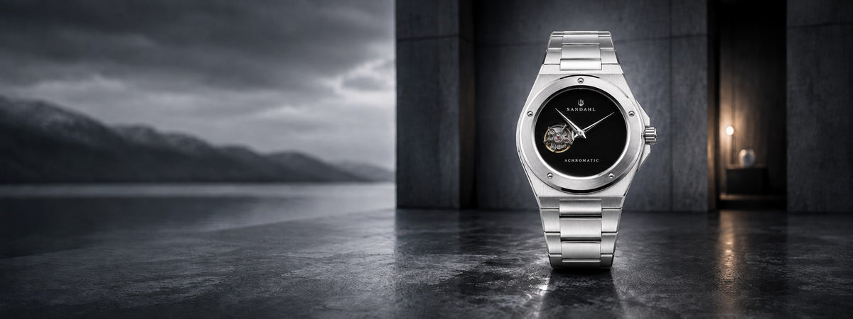 SANDAHL ACHROMATIC Musou with a steel bracelet in a dark architectural setting beside a misty lake.