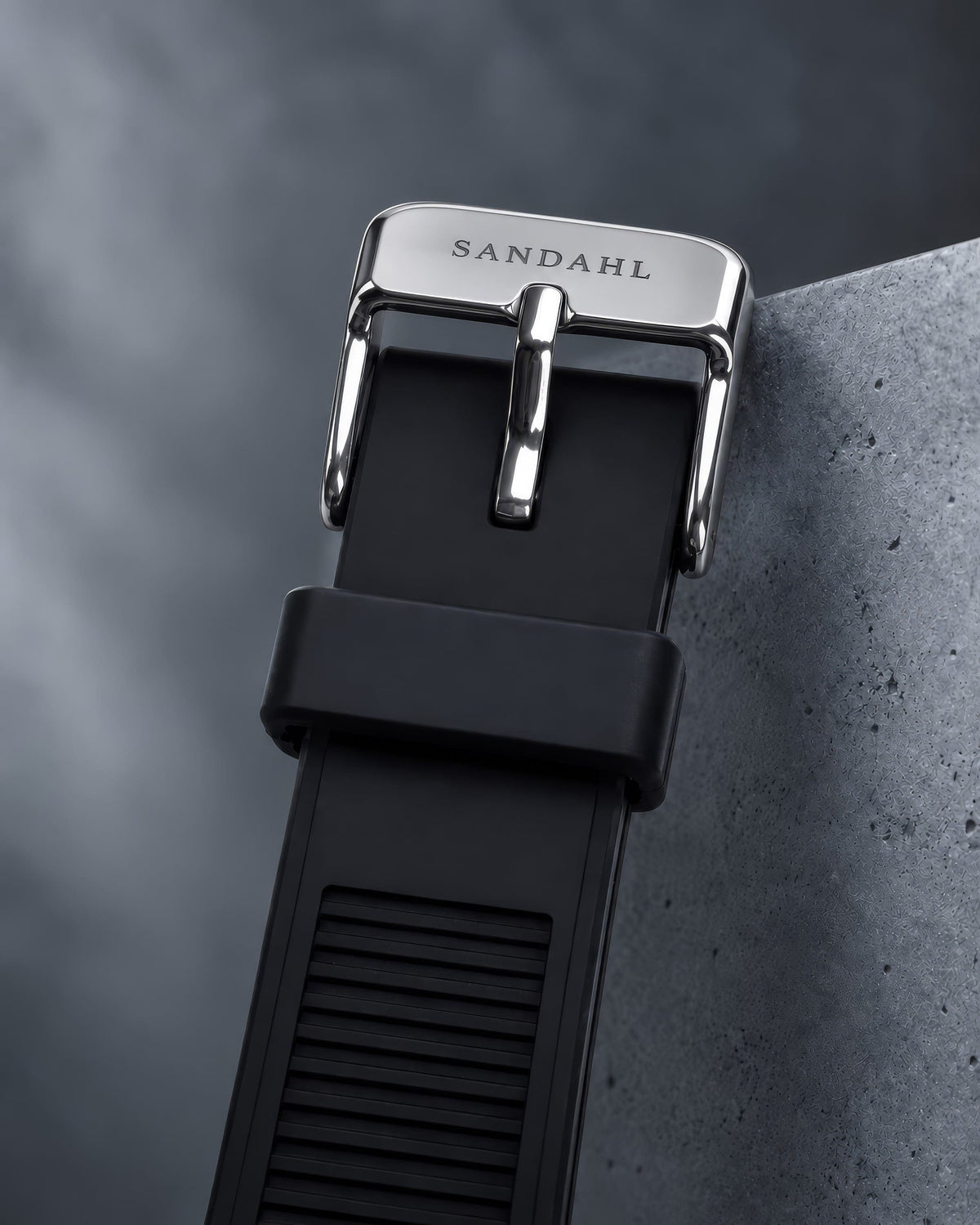Close-up of the SANDAHL ACHROMATIC black rubber strap and polished buckle engraved SANDAHL.