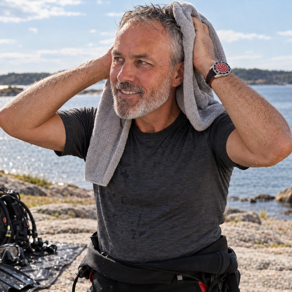 Man drying his hair after a dive in the Swedish archipelago, wearing a SANDAHL CENTURION Signal Red watch.