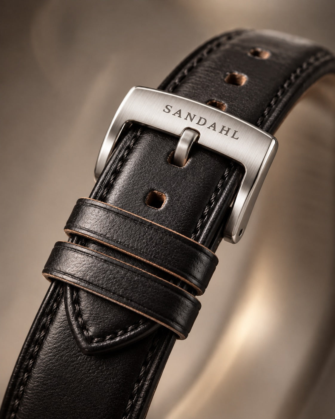 Close-up of a black Horween leather watch strap with matching stitching and a brushed stainless steel buckle engraved SANDAHL.