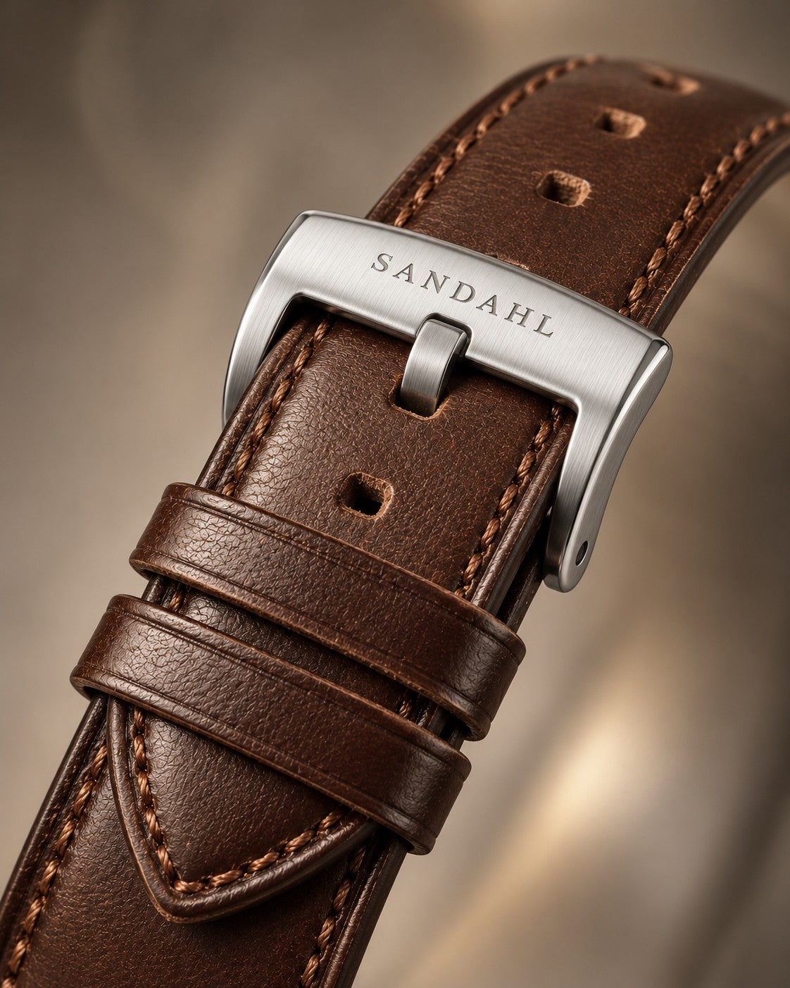 Close-up of a brown Horween leather watch strap with matching stitching and a brushed stainless steel buckle engraved SANDAHL.