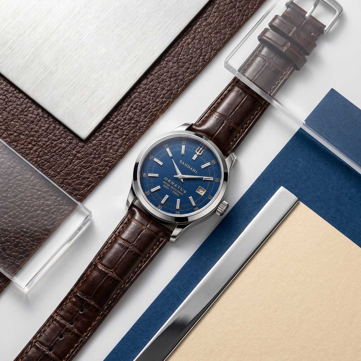 SANDAHL ORNATUS Cobalt with a blue dial, polished steel case and brown crocodile-pattern leather strap, arranged with blue, leather and metal material samples.