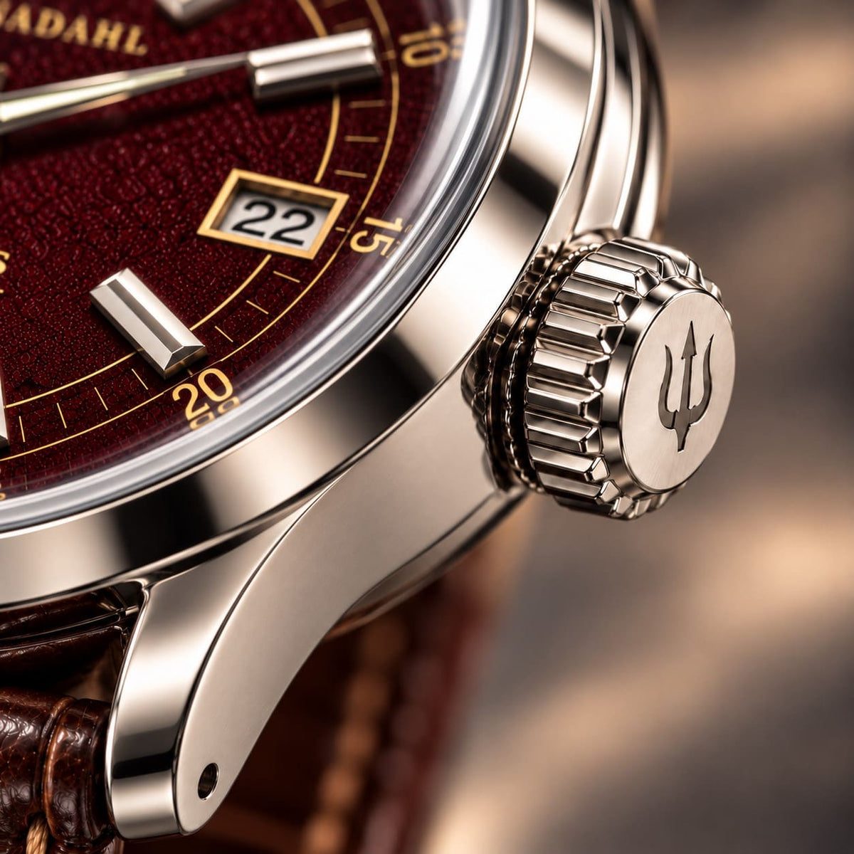 Close-up of the grooved steel crown with engraved trident on SANDAHL ORNATUS Garnet, beside the burgundy-red dial and polished case.