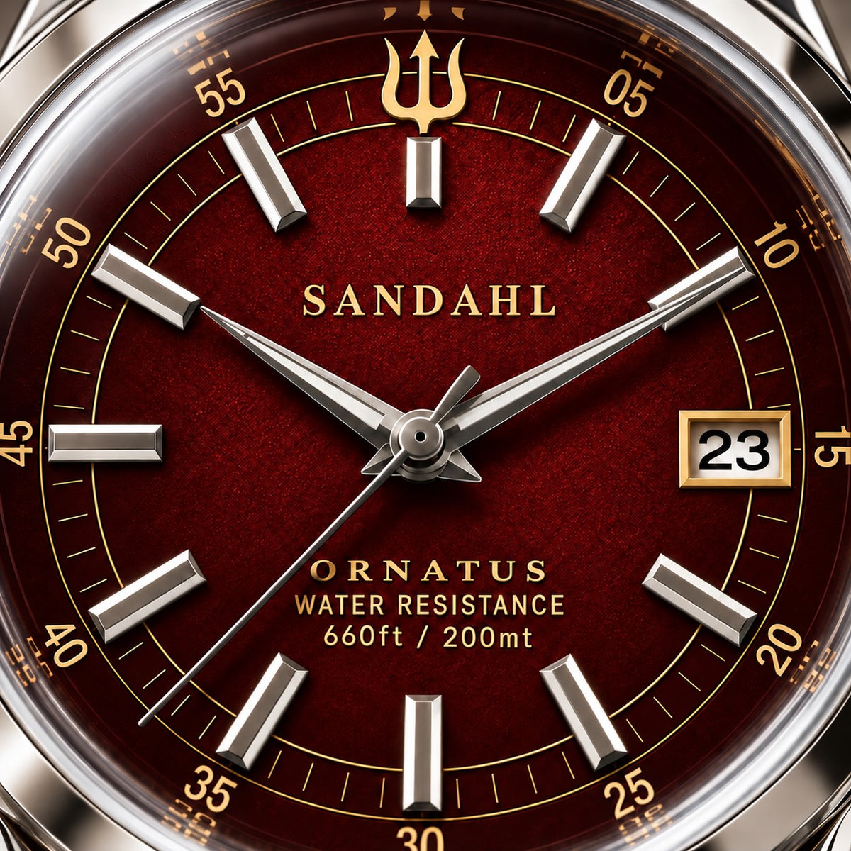 Macro view of the textured burgundy-red dial of SANDAHL ORNATUS Garnet, with polished hands, applied hour markers and a gold trident.