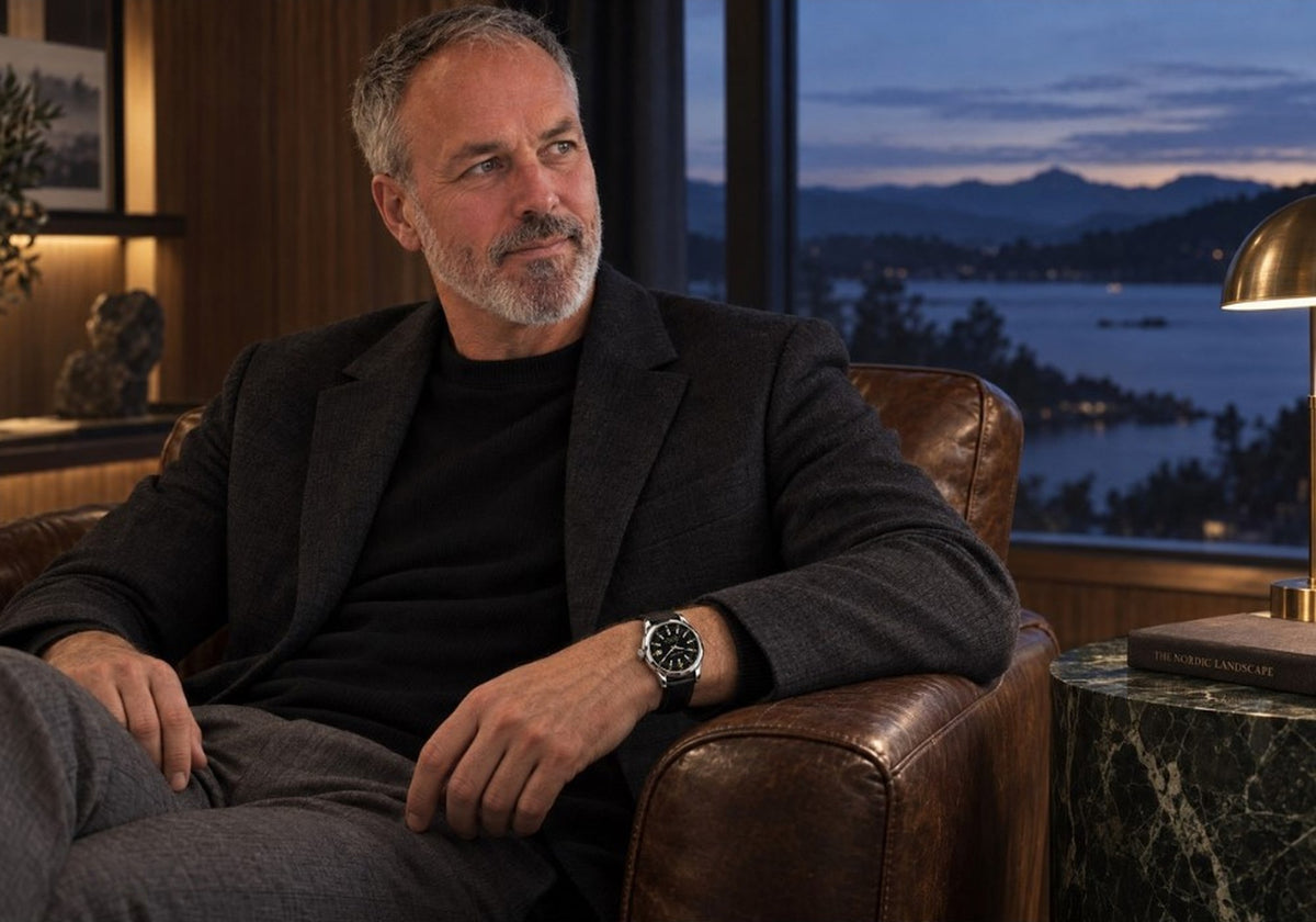 Man wearing a SANDAHL ORNATUS Onyx watch with a black dial while seated in a leather armchair in a waterfront lounge at dusk.