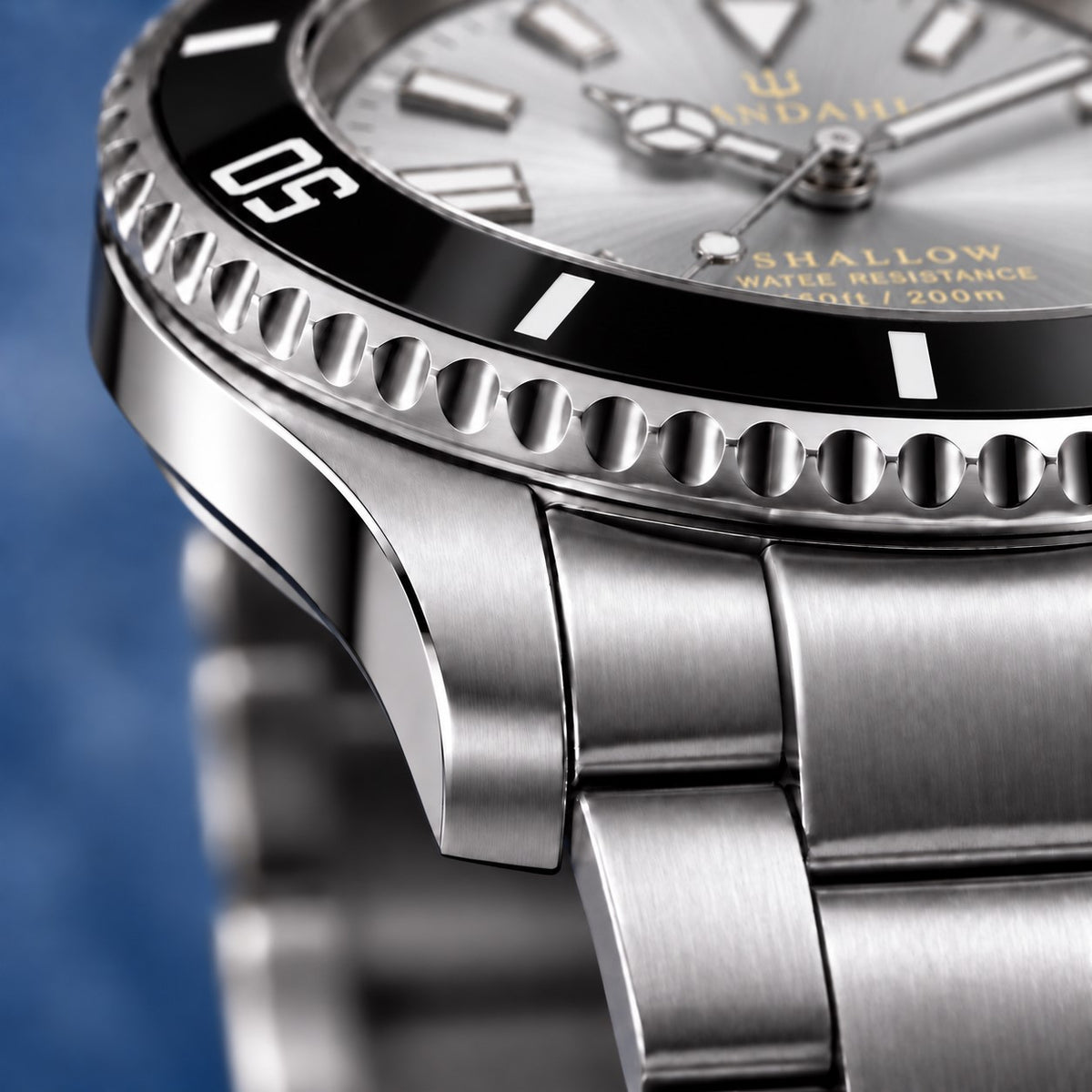 Macro view of the SANDAHL SHALLOW Sea Mist Silver steel case and bracelet, with a black dive bezel and silver dial.