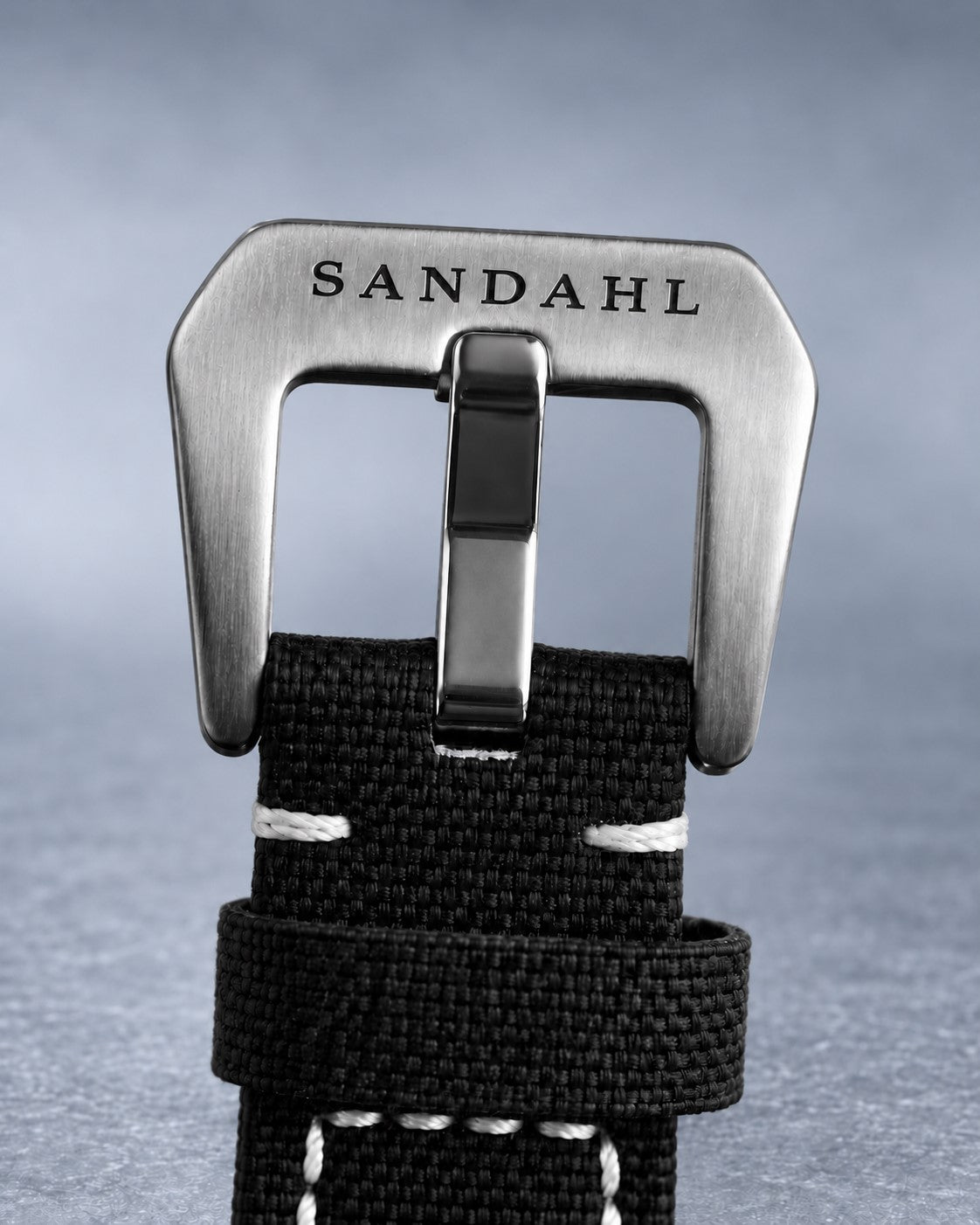 Close-up of the engraved steel buckle and stitched fabric strap on SANDAHL SHALLOW Sea Mist Silver.