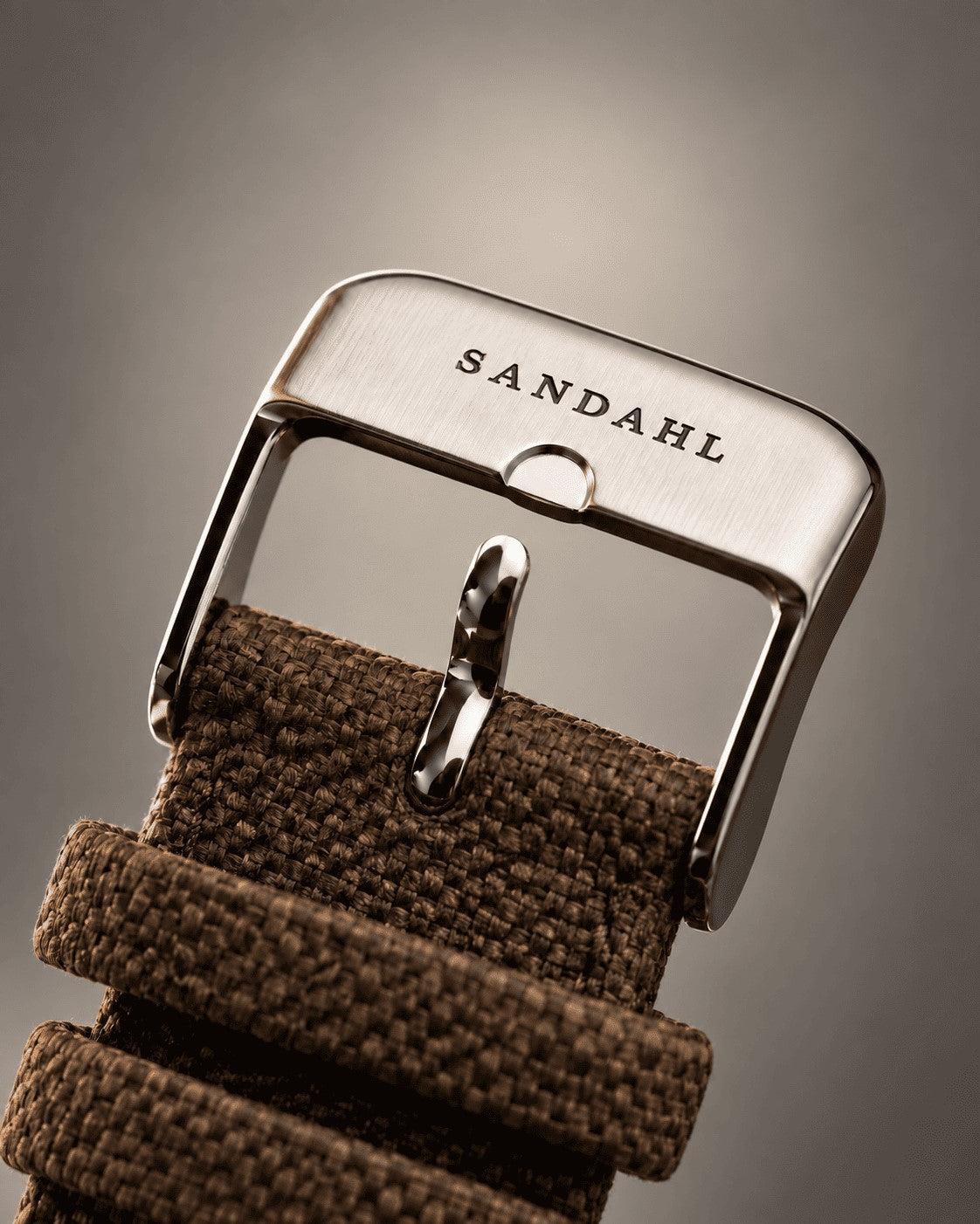 Close-up of the SANDAHL-engraved steel buckle and brown textile strap for SUITS.