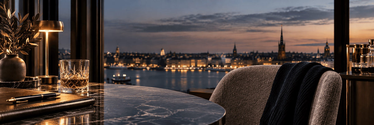 Warmly lit dining interior overlooking a waterfront city at dusk.